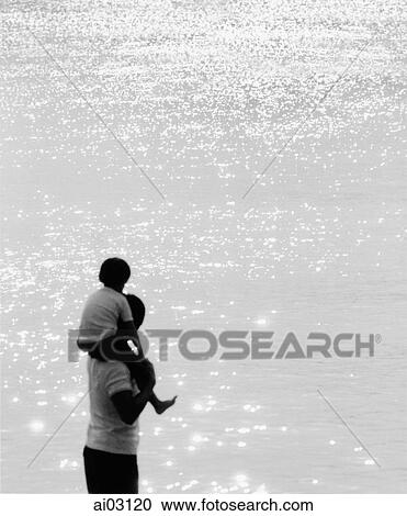 Stock Image - Father and son standing on beach, son on father's shoulders. Fotosearch