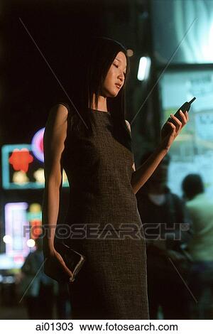 Stock Image - Female executive dialing cellular phone with neon in background. Fotosearch