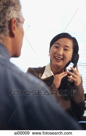 Female executive holding telephone talking with Caucasian male executive View Large Photo Image Stock Photo - Female executive holding telephone talking with Caucasian male executive. Fotosearch