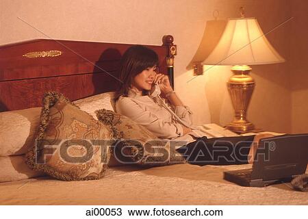 Stock Image - Female executive in hotel room talking on phone, with laptop computer. Fotosearch
