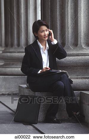 Stock Image - Female executive sitting, using cellular phone. Fotosearch
