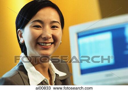 Female executive smiling with computer monitor in background View Large Photo Image Stock Image - Female executive smiling with computer monitor in background. Fotosearch