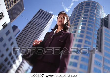 Stock Photo - Female executive standing in front of high-rise buildings, low angle view. Fotosearch