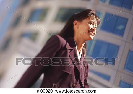 Stock Image - Female executive with office building behind, low angle view. Fotosearch