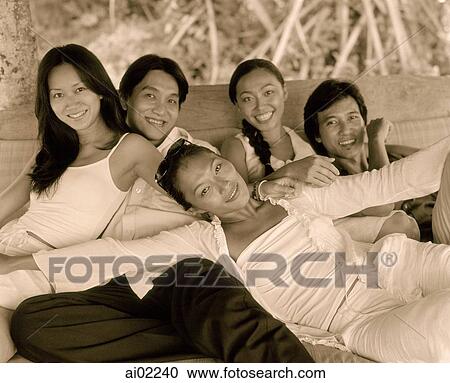 Stock Image - Friends sitting together, laughing on couch, woman in front with arms outstretched, outdoors. Fotosearch