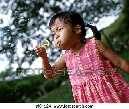 Girl blowing bubbles, tree in background View Large Photo Image Picture - Girl blowing bubbles, tree in background. Fotosearch