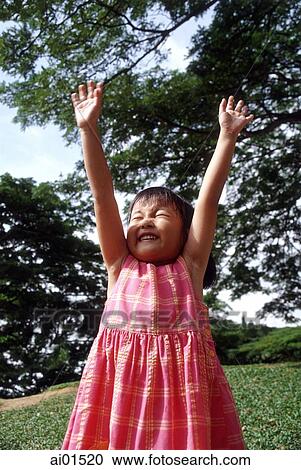 Stock Image - Girl stretching arms up, tree in background. Fotosearch