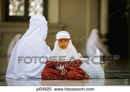 Indonesia, Aceh, Banda Aceh, Muslim girl dressed in mukenahs or kerudungs (prayer robes) sits with mother at Baiturrahman Great Mosque. View Large Photo Image Stock Image - Indonesia, Aceh, Banda Aceh, Muslim girl dressed in mukenahs or kerudungs (prayer robes) sits with mother at Baiturrahman Great Mosque.. Fotosearch