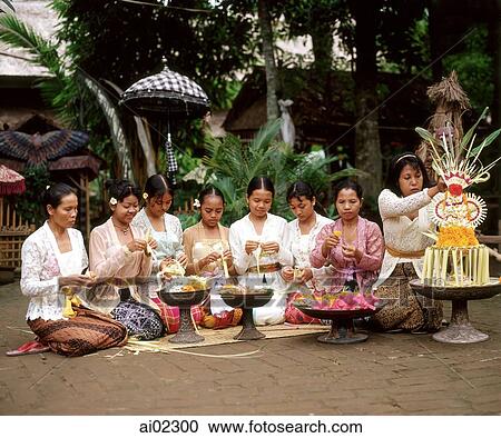 Stock Image - Indonesia, Bali, Balinese women and girls in traditional costume making floral arrangements. Fotosearch