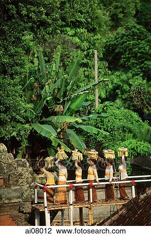 Stock Image - Indonesia, Bali, Gianyar, Cremation ceremony, women carrying offerings entering temple via bamboo bridge. (grainy). Fotosearch