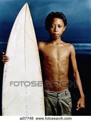 Indonesia, Bali, Kuta Beach, Young surfer holding surfboard on the beach. View Large Photo Image Stock Photo - Indonesia, Bali, Kuta Beach, Young surfer holding surfboard on the beach.. Fotosearch