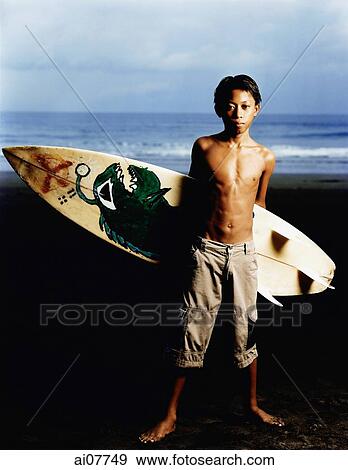 Indonesia, Bali, Kuta Beach, Young surfer holding surfboard on the beach. View Large Photo Image Stock Photo - Indonesia, Bali, Kuta Beach, Young surfer holding surfboard on the beach.. Fotosearch