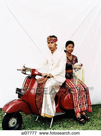 Indonesia, Bali, Ubud, Balinese wedding couple in ceremonial dress, sitting on motor scooter, woman carrying offering. View Large Photo Image Stock Photo - Indonesia, Bali, Ubud, Balinese wedding couple in ceremonial dress, sitting on motor scooter, woman carrying offering.. Fotosearch