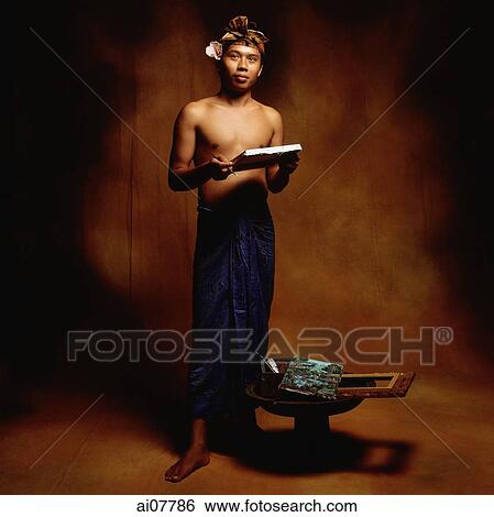 Stock Photograph - Indonesia, Bali, Ubud, Young Balinese man with his paintings of Bali scenery.. Fotosearch