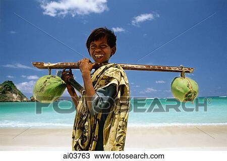 Stock Image - Indonesia, Lombok, boy selling coconuts on beach. Fotosearch