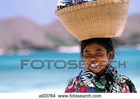 Picture - Indonesia, Lombok, Tanjung Aan, girl on beach, basket on head.. Fotosearch