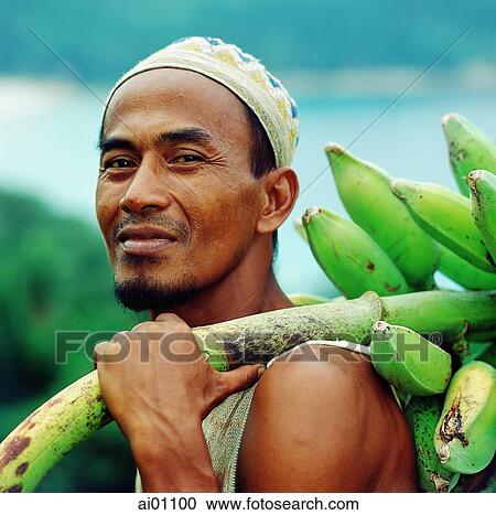 Stock Image - Malaysia, Terengganu State, Pulua Perhintian Kechil, local man holding a bunch of bananas. Fotosearch