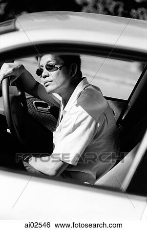 Male driver wearing sunglasses leaning forward in car to look out the windshield View Large Photo Image Stock Photograph - Male driver wearing sunglasses leaning forward in car to look out the windshield. Fotosearch