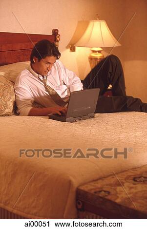Stock Image - Male executive in hotel room using laptop computer. Fotosearch