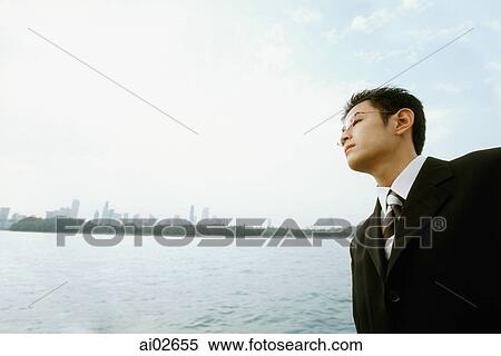 Male executive looking across water, blue sky in background View Large Photo Image Stock Photography - Male executive looking across water, blue sky in background. Fotosearch