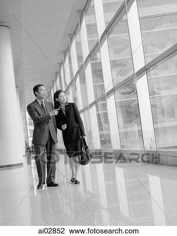 Male executive pointing out something to female while walking down hall. View Large Photo Image Stock Image - Male executive pointing out something to female while walking down hall.. Fotosearch
