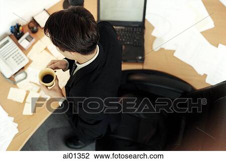 Stock Image - Male executive sitting at desk, top view.. Fotosearch
