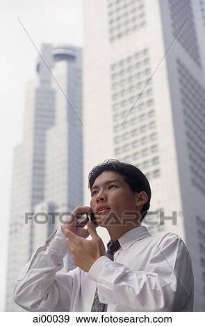 Male executive talking on cellular phone with office buildings behind, low angle view View Large Photo Image Stock Photo - Male executive talking on cellular phone with office buildings behind, low angle view. Fotosearch