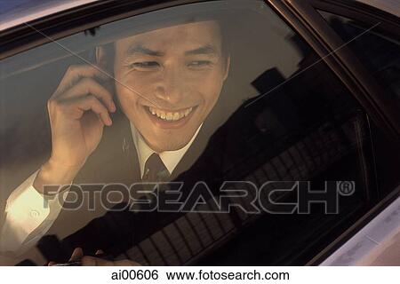 Stock Photograph - Male executive using cellular phone in car, smiling. Fotosearch