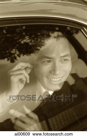 Stock Photo - Male executive using cellular phone hands-free set in car, smiling. Fotosearch