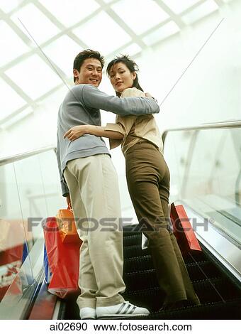 Man and woman carrying shopping bags going upward on escalator looking back. View Large Photo Image Stock Image - Man and woman carrying shopping bags going upward on escalator looking back.. Fotosearch