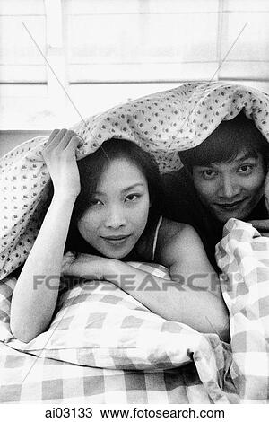 Stock Image - Man and woman in bed under sheet, portrait. Fotosearch