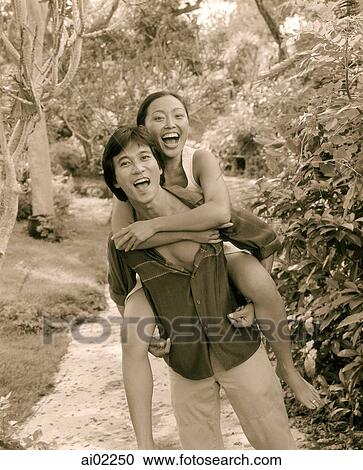 Stock Image - Man carrying woman on back, laughing. Fotosearch