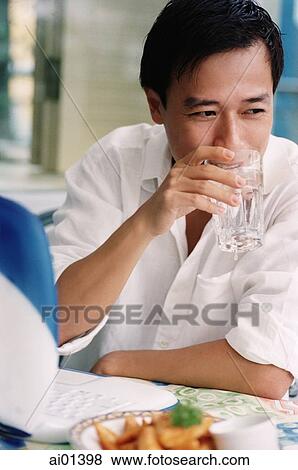 Stock Photo - Man drinking water, laptop in front of him. Fotosearch