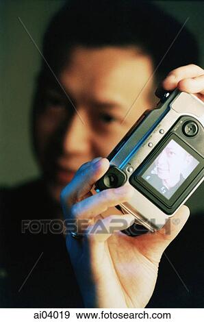 Stock Photo - Man holding digital camera, black background. Fotosearch
