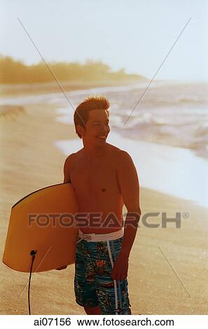 Man holding surf board by beach View Large Photo Image Stock Photograph - Man holding surf board by beach. Fotosearch