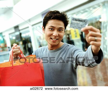Man holding up credit card and shopping bags, shops in background, portrait. View Large Photo Image Stock Image - Man holding up credit card and shopping bags, shops in background, portrait.. Fotosearch