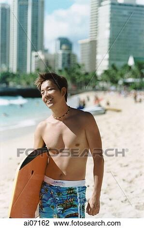 Stock Image - Man holding wakeboard by beach ( high grain). Fotosearch