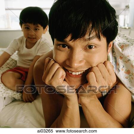 Stock Photography - Man in bed, son in background, portrait. Fotosearch