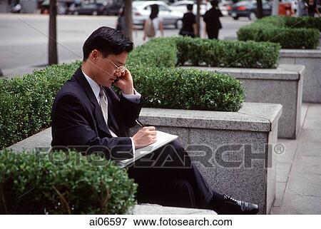 Stock Photo - Man in business suit, using mobile phone and writing on note pad. Fotosearch