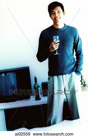 Stock Photo - Man in living room holding a wine glass, portrait. Fotosearch