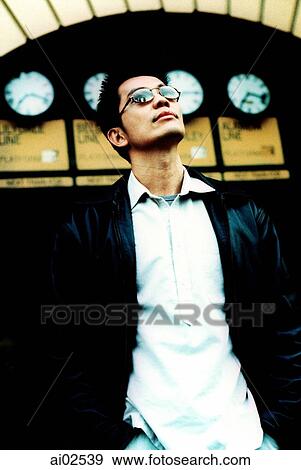 Stock Photo - Man in sunglasses looking up, archway with clocks in background. Fotosearch
