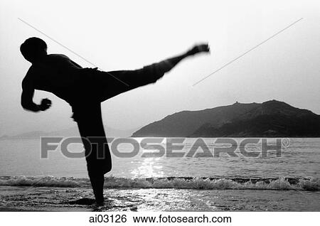 Stock Photograph - Man kicking in Kung Fu (Wu Shu) pose on beach, silhouette. Fotosearch