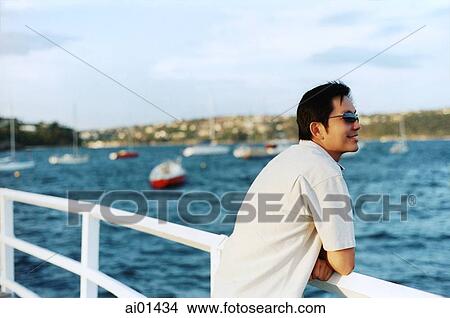 Man leaning on railing looking out at water View Large Photo Image Picture - Man leaning on railing looking out at water. Fotosearch