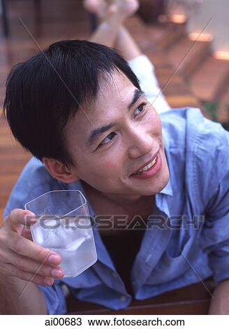 Man lying down holding glass of drink, looking off camera View Large Photo Image Stock Image - Man lying down holding glass of drink, looking off camera. Fotosearch
