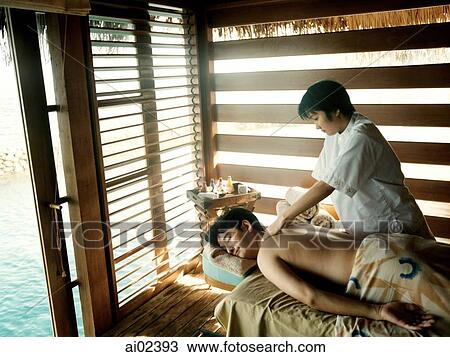 Stock Image - Man receiving massage from woman, water in background.. Fotosearch
