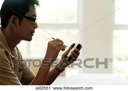Stock Image - Man sitting at table using PDA, white background. Fotosearch