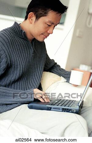 Man sitting cross-legged using laptop holding cup View Large Photo Image Picture - Man sitting cross-legged using laptop holding cup. Fotosearch
