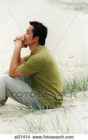Picture - Man sitting on beach resting chin on hands. Fotosearch