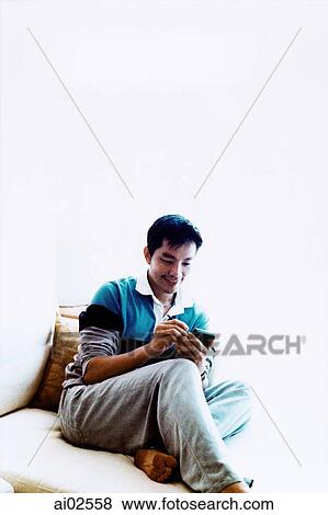 Man sitting on sofa using PDA View Large Photo Image Stock Photo - Man sitting on sofa using PDA. Fotosearch