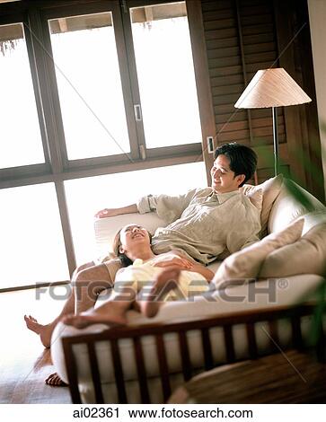 Stock Image - Man sitting on sofa, woman lying down with head on lap. Fotosearch